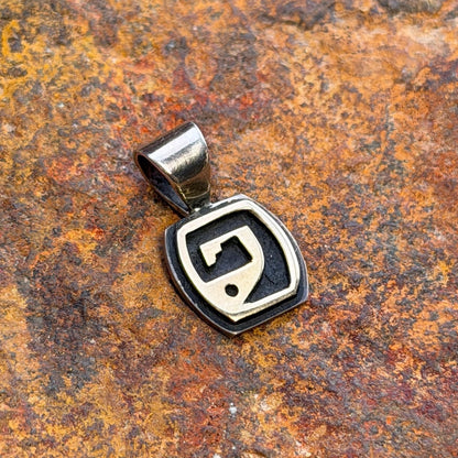 a sterling silver pendant with a gold overlayed geometric design on a oxidized dark sterling silver pendant. it rests on an orange rust colored rock.