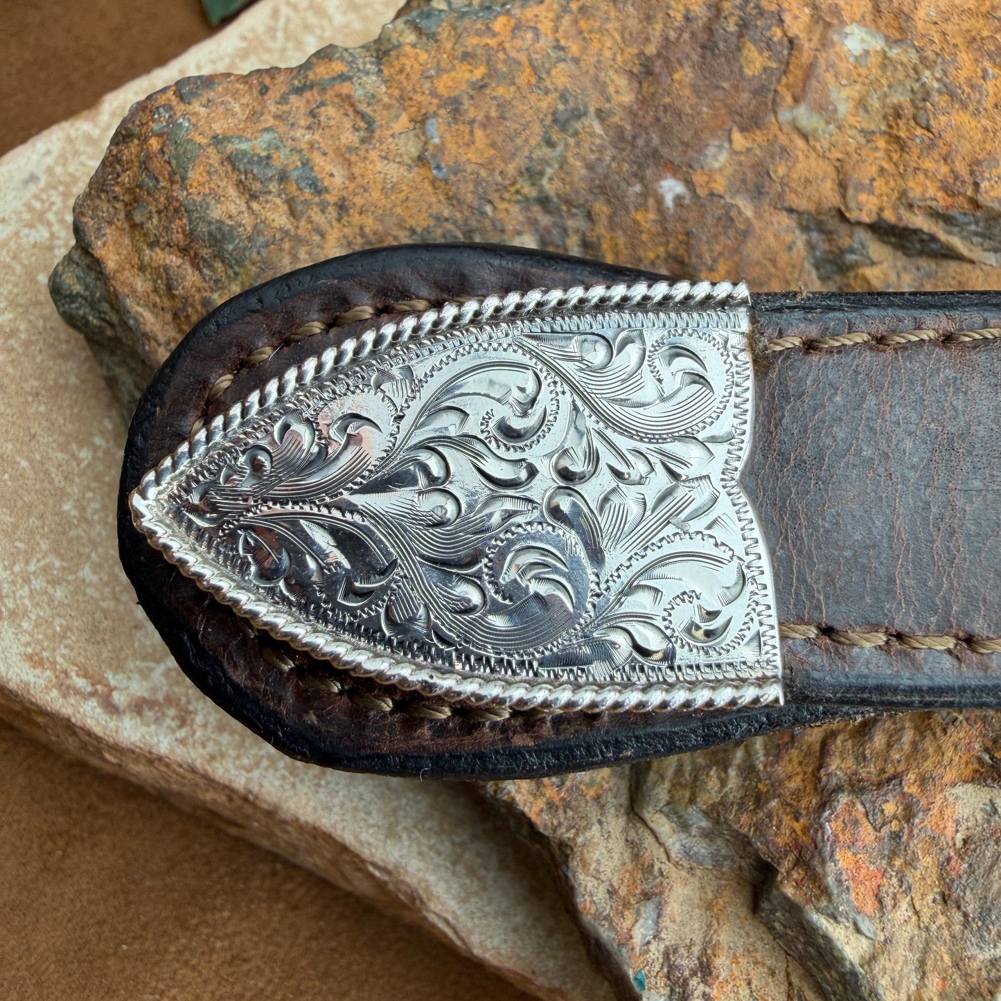 Decorative knife sheath with intricate silver design on a stone surface
