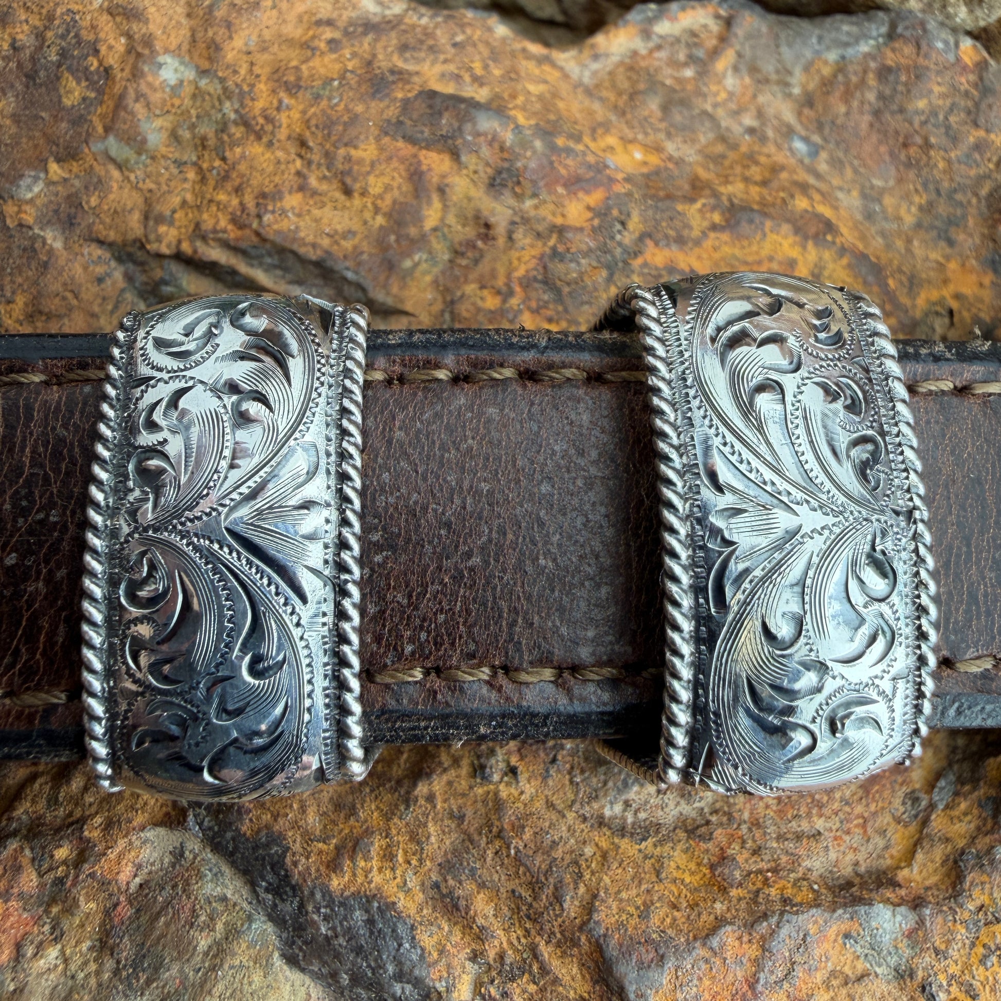 Decorative leather belt with silver buckle on a stone background