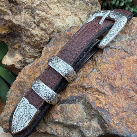 Decorative belt with brown leather sheath and silver metalwork on a stone surface