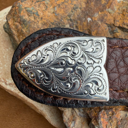 Decorative silver belt buckle on a brown leather belt against a stone background