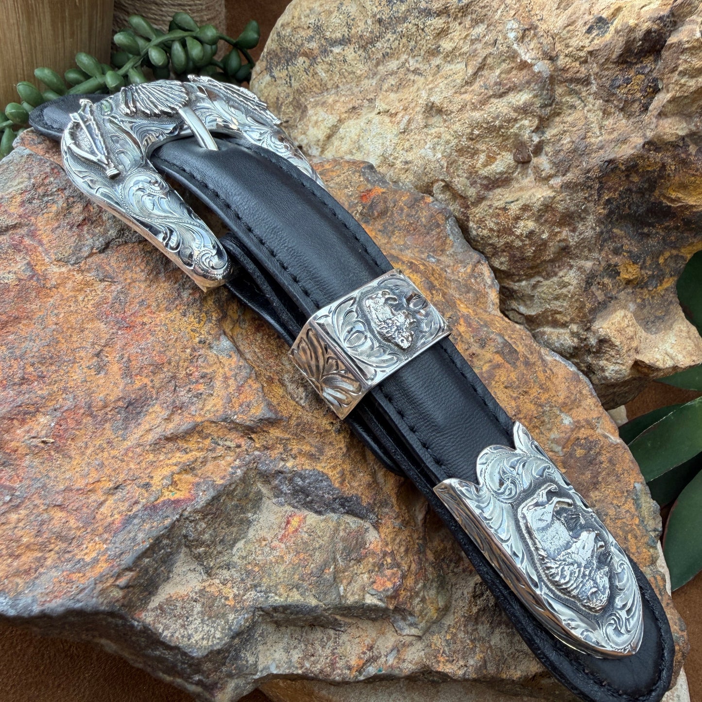 Decorative belt buckle with silver blade and black sheath on a stone surface