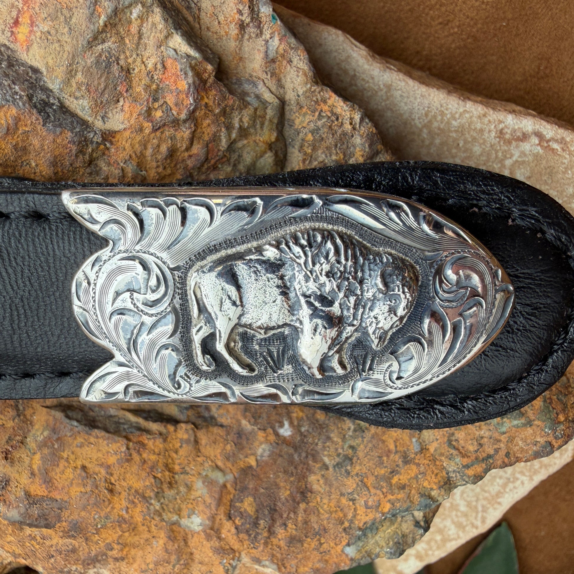 Belt with a silver buckle featuring a buffalo design on a rocky surface