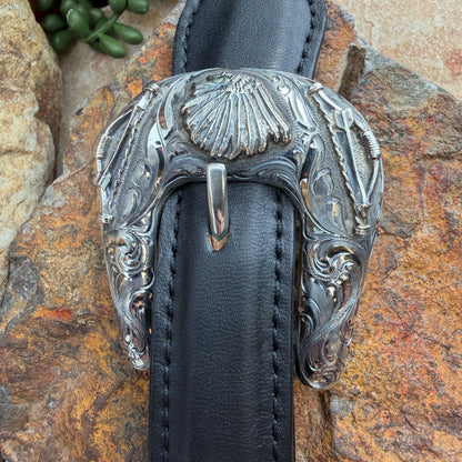 Decorative silver buckle on a black leather strap against a stone background