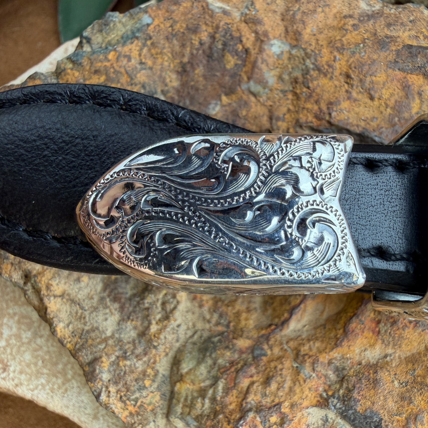 Decorative silver belt buckle on a black belt against a stone background