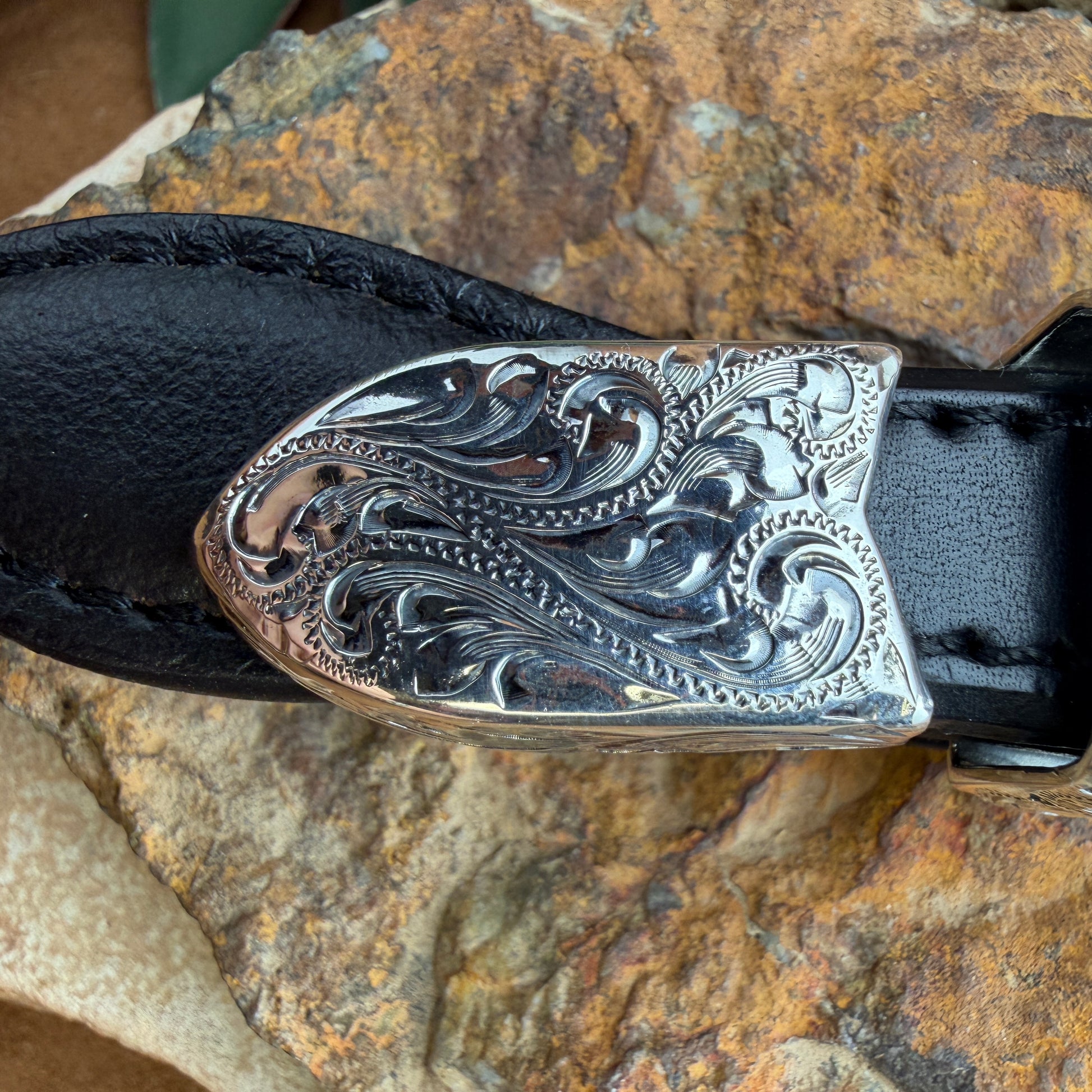 Decorative silver belt buckle on a black belt against a stone background