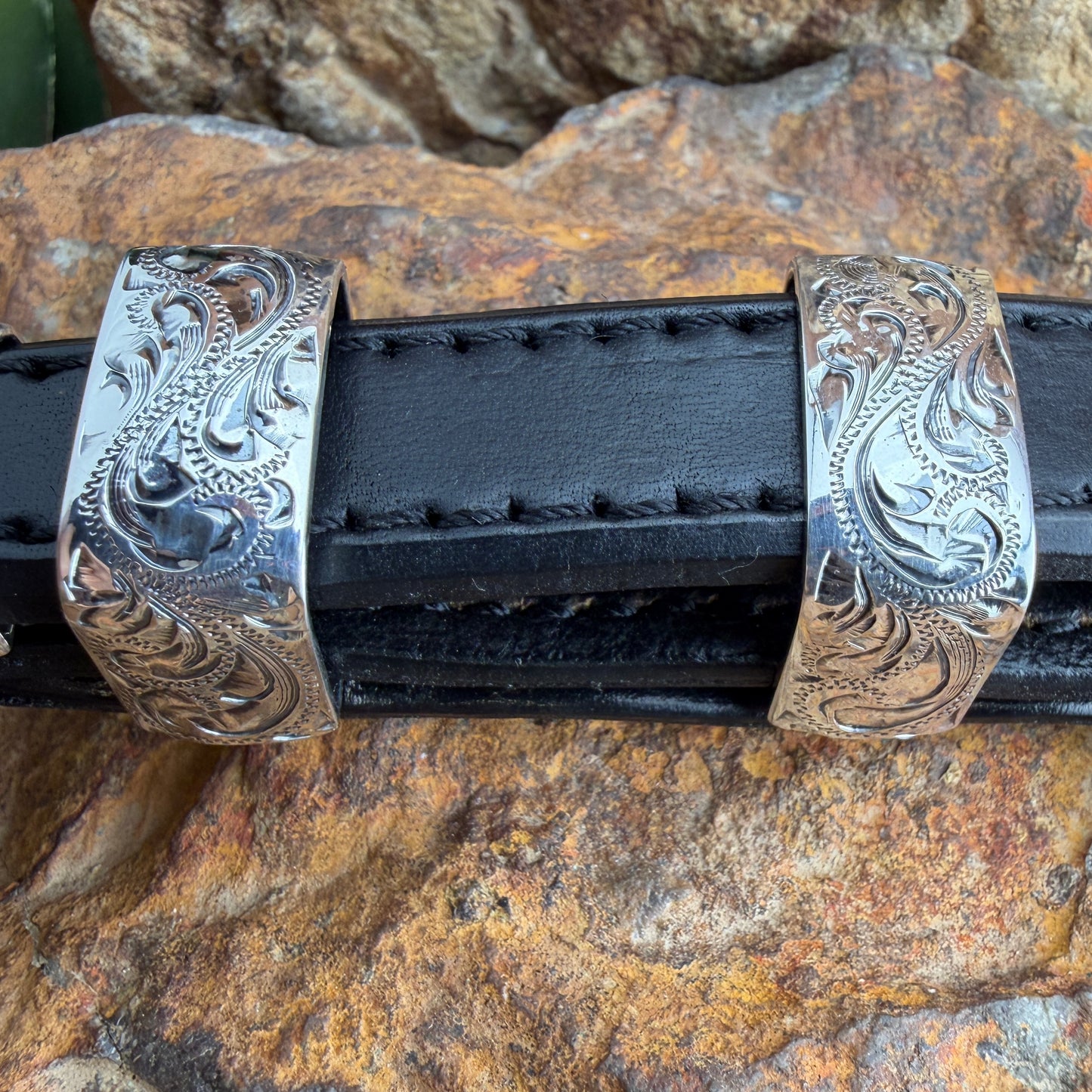 Decorative silver belt buckle on a black belt against a rocky background