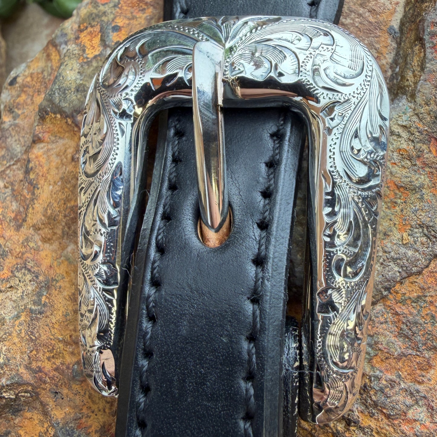 Close-up of a black leather belt with a silver buckle on a stone surface