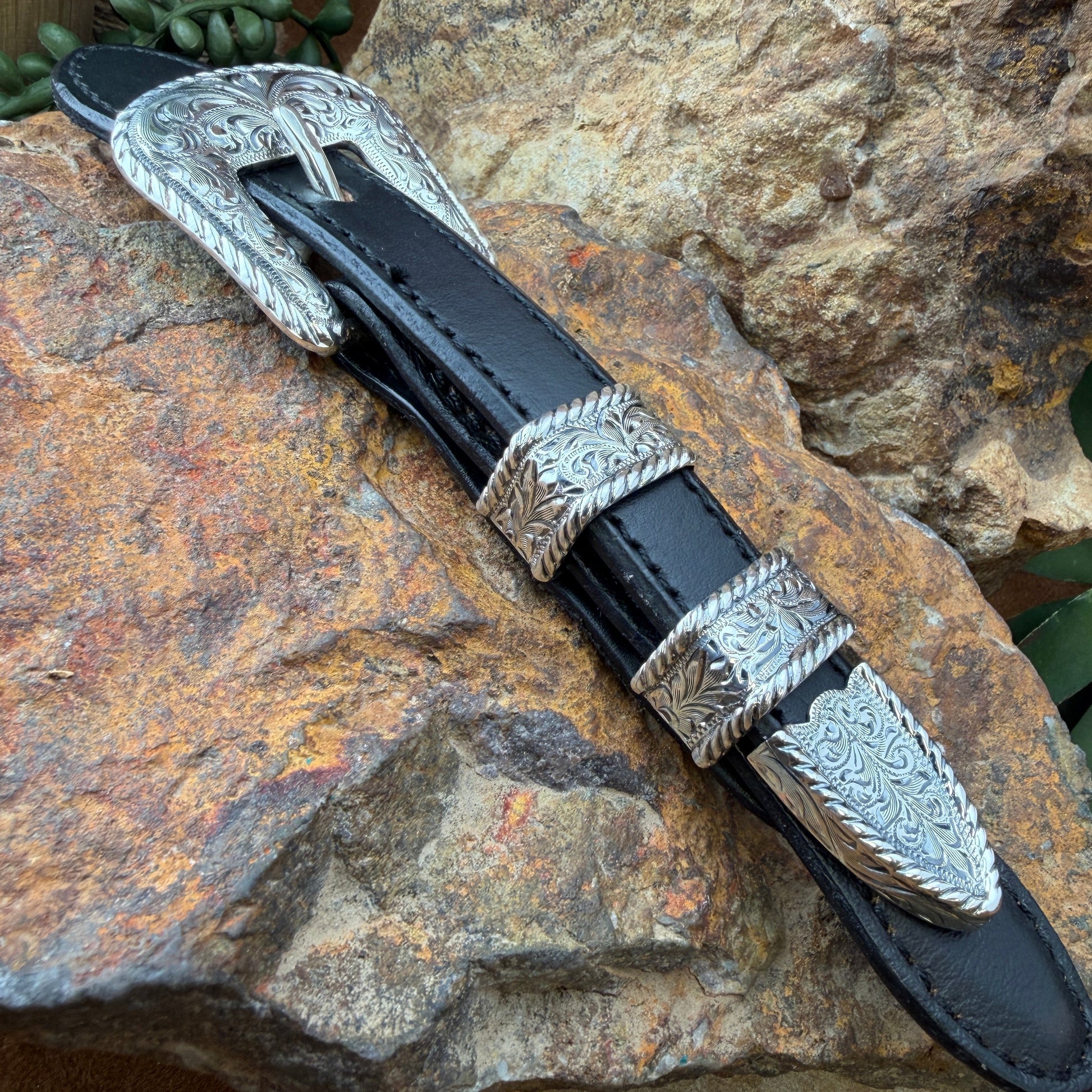 Black leather belt with silver buckle on a stone surface