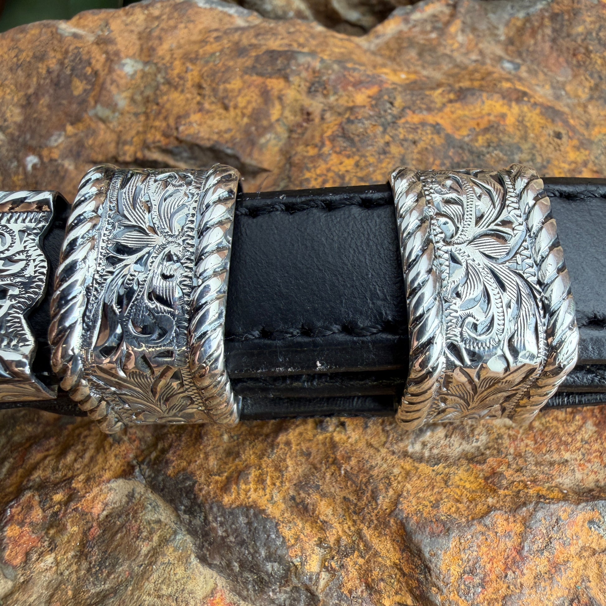 Black leather belt with silver floral buckle on a stone surface