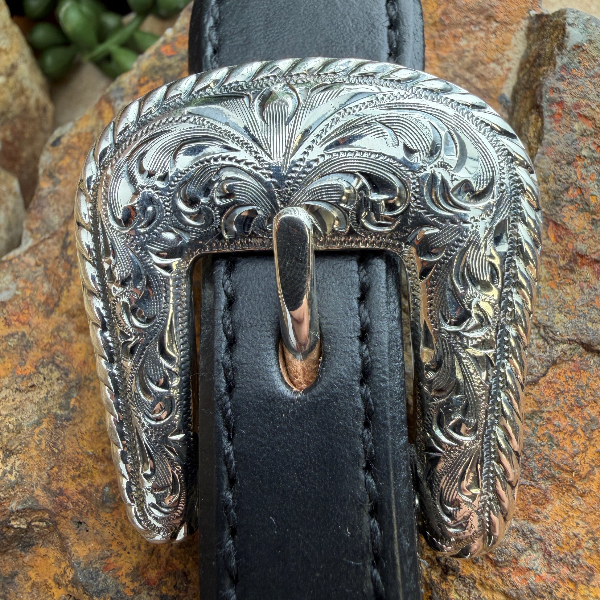 Decorative silver belt buckle on a black leather belt against a stone background