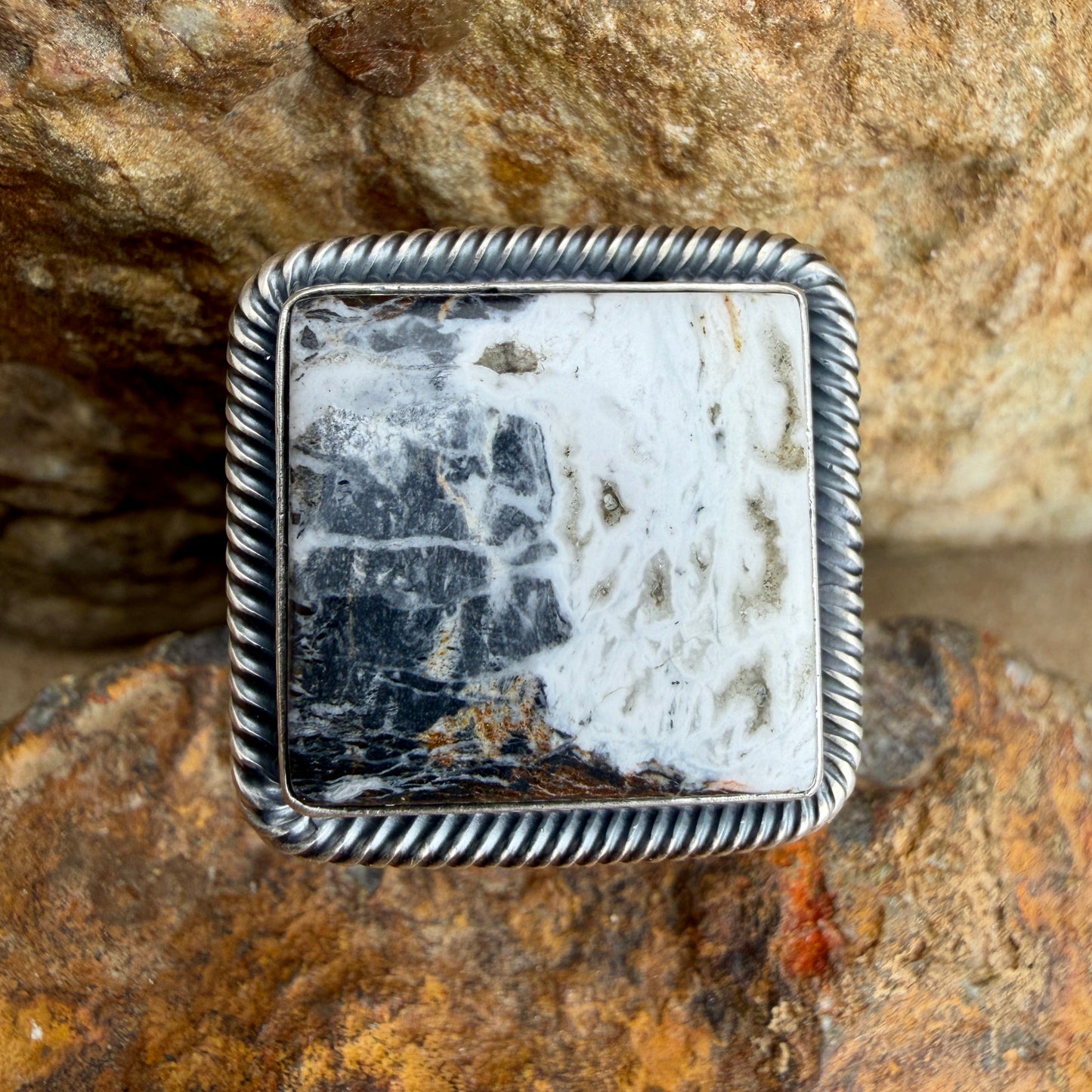 Silver ring with a white and black square stone on a textured stone background