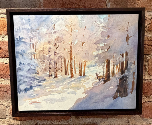 Framed painting of a winter landscape with a deer on a brick wall.