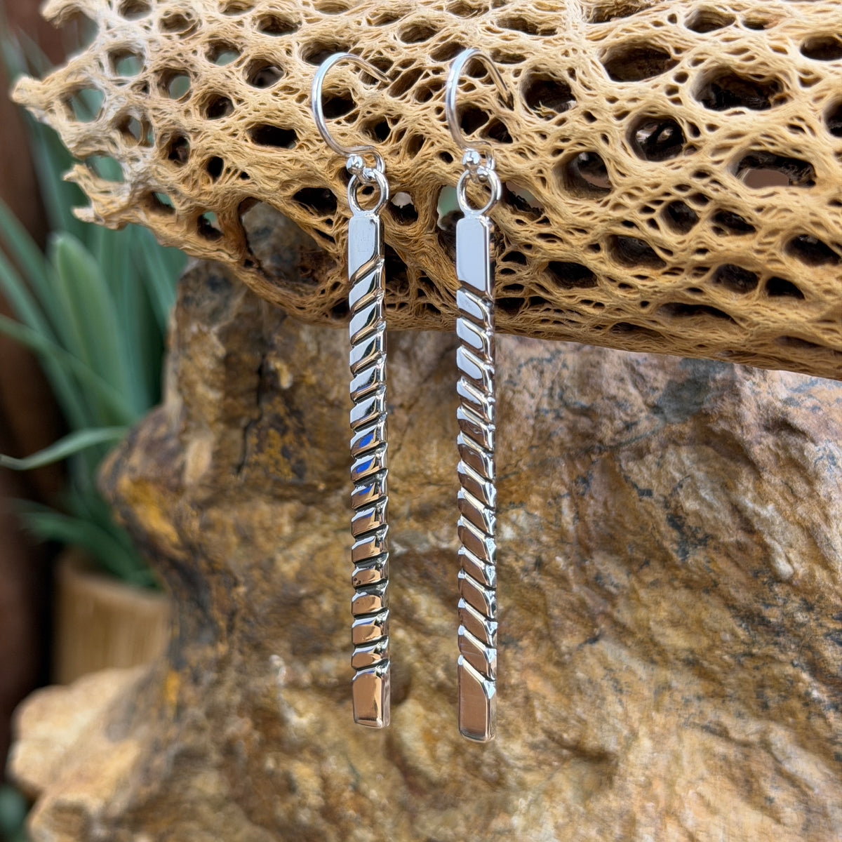elongated rectangle earrings with diagonal geometric line pattern by artie yellowhorse hanging from a piece of driftwood